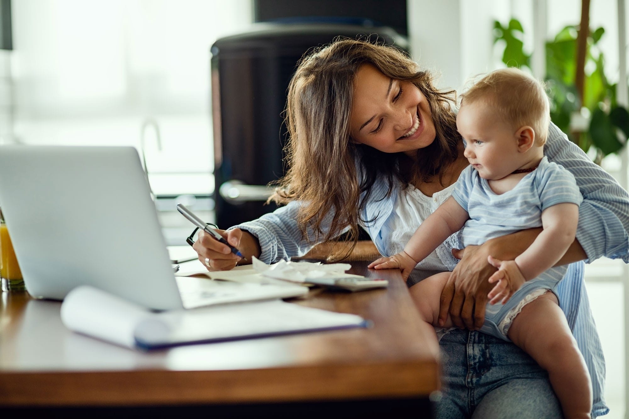 Imagen de una madre muy contenta trabajando en el ordenador con su bebé encima