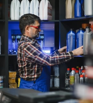 Imagen de un vendedor de una tienda de autopartes acomodando botellas de aceite de motor en un estante, asegurando una buena visibilidad del producto para los clientes
