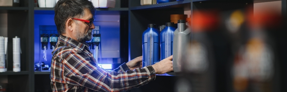 Imagen de un vendedor de una tienda de autopartes acomodando botellas de aceite de motor en un estante, asegurando una buena visibilidad del producto para los clientes