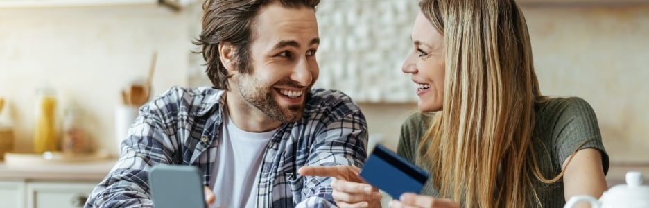 Imagen de un hombre alegre de haber sorprendido a la familia milenaria europea con teléfono y tarjeta de crédito, esposa rubia señalando con el dedo el gadget