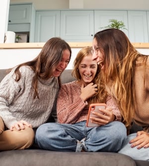 Imagen de un grupo de amigas en el sofá de casa, usando un teléfono móvil riéndose
