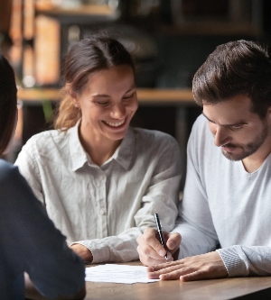 Imagen de una pareja milenaria emocionada reunida con una agente inmobiliaria o corredora en un café que firma un contrato comprando la primera propiedad juntos, los cónyuges felices firman el acuerdo de cierre con el banquero para tomar un préstamo