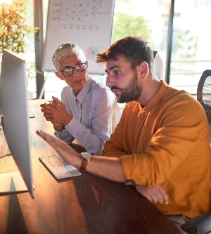 Imagen de un joven empresario enfocado siendo asesorado por una socia senior en la oficina