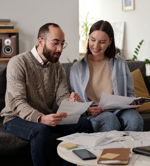 Imagen de un joven confiado señalando una factura financiera mientras estaba sentado en el sofá junto a su esposa sonriente y explicando sus datos en un documento.