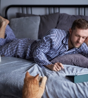 Imagen de un joven caucásico barbudo en pijama por la mañana acostado en una cama haciendo compras en línea o educando desde casa dos gatos atigrados sentados cerca imagen de alta calidad