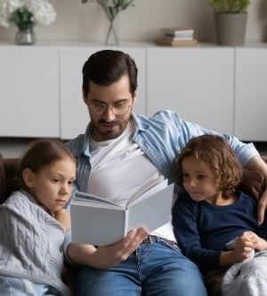 Imagen de un padre leyendo un libro a sus dos hijos en el salón de casa
