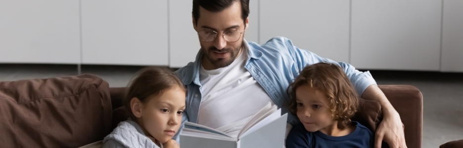 Imagen de un padre leyendo un libro a sus dos hijos en el salón de casa