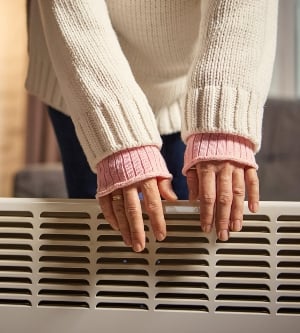 Imagen de una mujer de pie junto a un calefactor calentándose las manos en un acogedor apartamento moderno