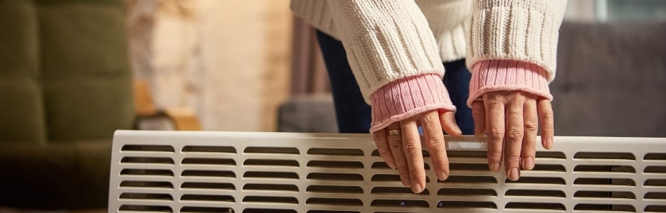 Imagen de una mujer de pie junto a un calefactor calentándose las manos en un acogedor apartamento moderno