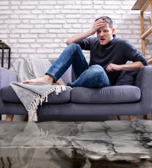 Imagen de un hombre sentado en el sofá de su casa mientras se hunde todo con agua