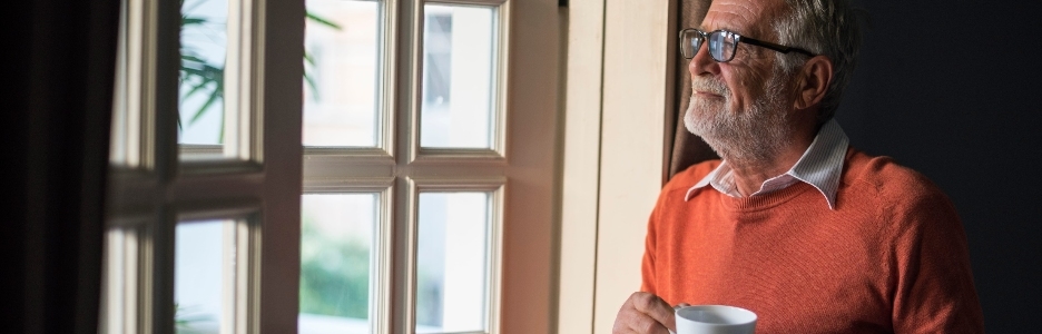 Imagen de un hombre con una taza de té apreciando la brisa que entra en su casa