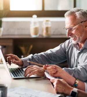 Imagen de una pareja de ancianos sentada en la cocina, usando la computadora y sonriendo