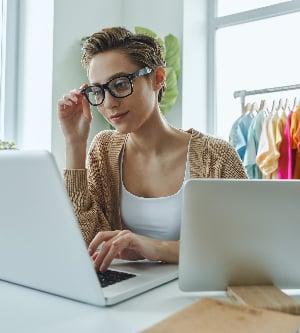 Imagen de una mujer joven segura que usa una computadora portátil mientras trabaja en la oficina de una tienda de moda