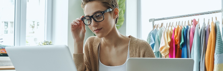 Imagen de una mujer joven segura que usa una computadora portátil mientras trabaja en la oficina de una tienda de moda