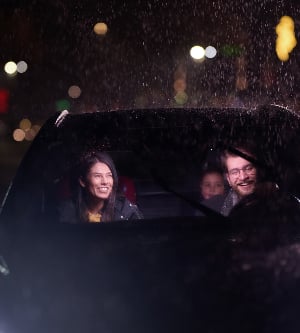 Imagen de un viaje nocturno, una familia feliz disfruta de momentos divertidos dentro de un automóvil mientras viajan a través de un clima lluvioso iluminado por el resplandor de los faros, risas y unión.