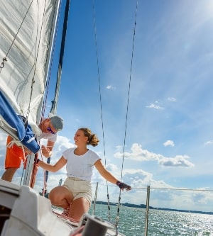 Joven y mujer navegando en un yate. Tripulante de velero femenino recortando la vela principal durante la navegación de vacaciones en temporada de verano