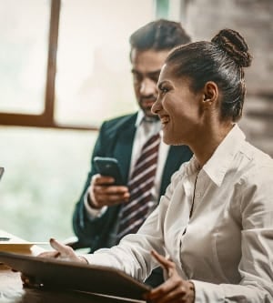 Mujer de negocios sonriente que sostiene una tableta digital, vista lateral de una encantadora oficinista que sonríe con dientes durante una conversación con sus compañeros de trabajo en una reunión de negocios, tiro en ángulo holandés, imagen tonificada