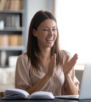 Imagen de una mujer joven muy contenta mirando la pantalla de la computadora portátil, sorprendida por las buenas noticias, mirando la pantalla de la computadora portátil, sentada en el escritorio de trabajo en casa, mujer emocionada celebrando el éxito, aplaudiendo, ganando en línea