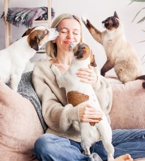 Imagen de una mujer jugando con sus perros y gatos en el salón de su casa