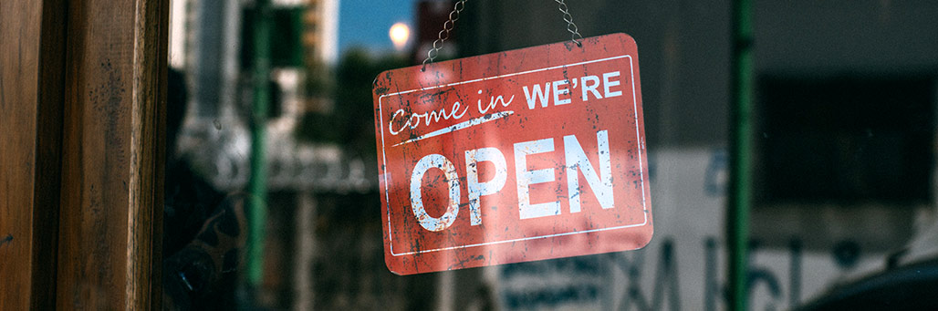 Imagen de una tienda con un cartel en la puerta que pone 'Estamos Abierto' en ingles