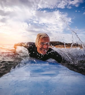 Imagen de un hombre de mayor edad surfeando en la playa
