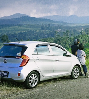 Imagen de un coche aparcado en una parada en las montañas mientras dos personas toman un descanso