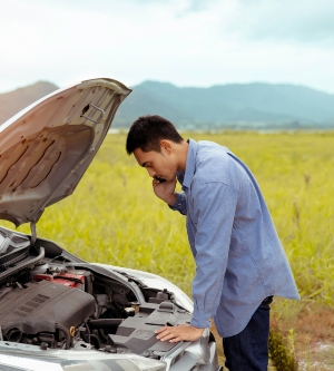 Imagen de un hombre solicitando asistencia para su coche mientras intenta resolver el problema en la carretera