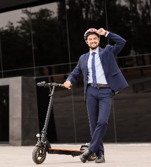 Imagen de un joven y apuesto empresario con casco en patinete eléctrico cerca de un edificio de oficinas