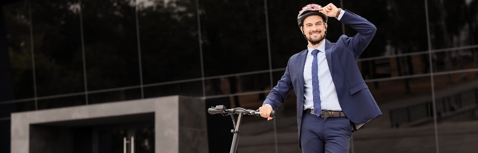 Imagen de un joven y apuesto empresario con casco en patinete eléctrico cerca de un edificio de oficinas