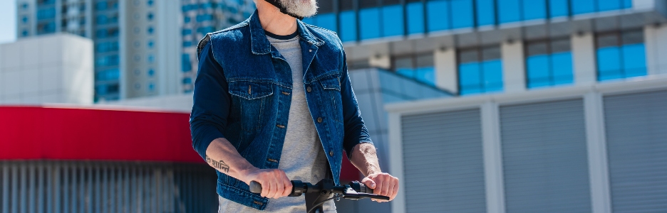Imagen de hombre positivo y maduro con casco y gafas de sol conduciendo un patinete eléctrico en la calle de la ciudad