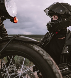 Imagen de mujer motociclista confiada en casco sentada cerca de la bicicleta. Motorista joven conductor al aire libre al atardecer.