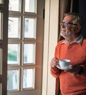 Imagen de un hombre con una taza de té apreciando la brisa que entra en su casa