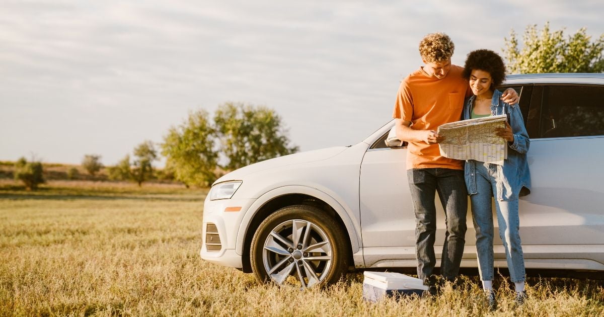 Image of a young multiracial couple smiling and examining map during car trip