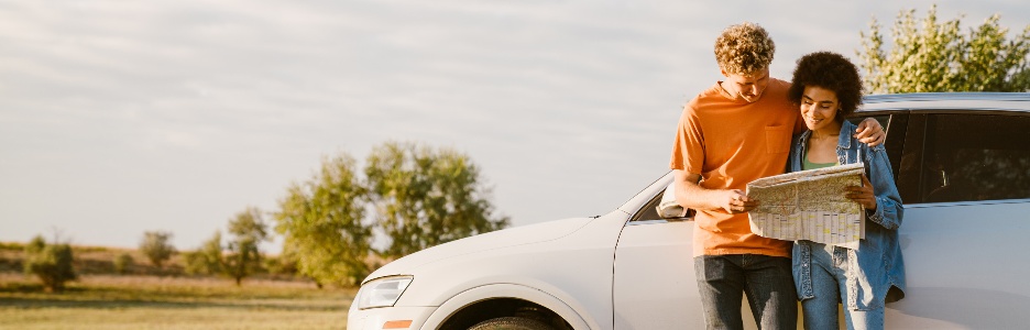 Image of a young multiracial couple smiling and examining map during car trip