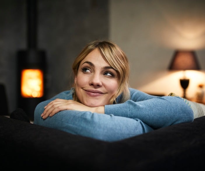 Imagen de una mujer sonriendo desde el sofá de su casa