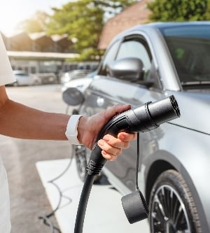 Imagen de una persona sosteniendo un enchufe de carga para coche eléctrico en una estación de carga en la ciudad