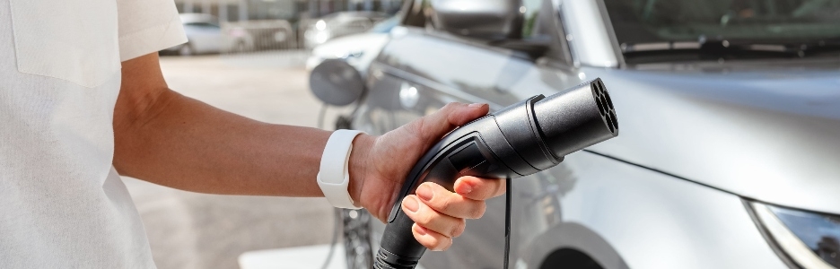 Imagen de una persona sosteniendo un enchufe de carga para coche eléctrico en una estación de carga en la ciudad