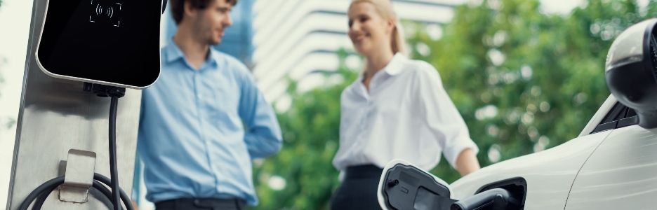 Imagen de enfoque el estacionamiento: automóvil eléctrico conectado a la estación de carga pública con desenfoque progresivo de empresarios tomando café, fondo de apartamento y condominio de edificio residencial para un concepto ecológico.