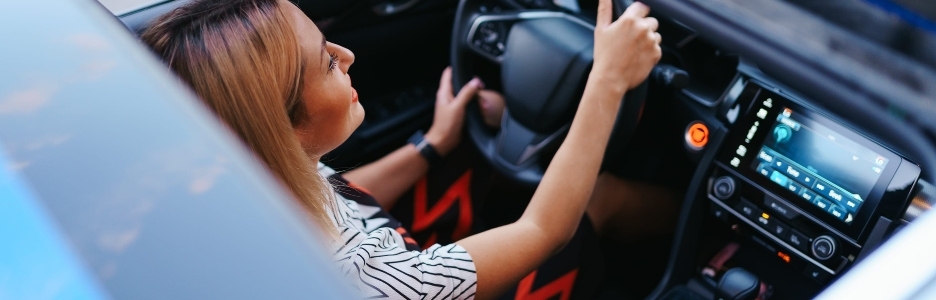 Imagen de una mujer joven conduciendo con techo corredizo abierto