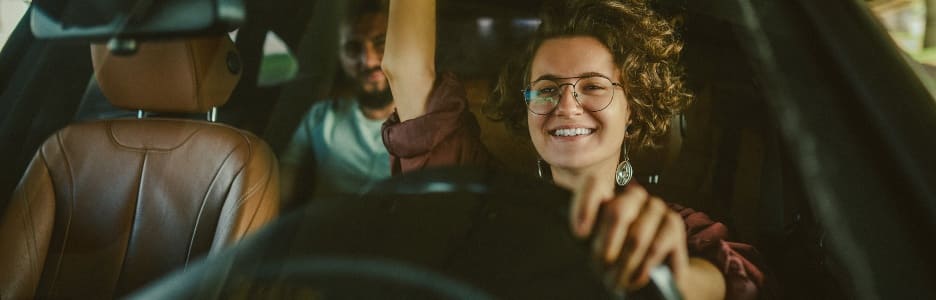 Imagen de una mujer de cabello rizado conduciendo un auto y luciendo contenta