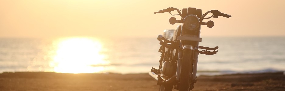 Imagen de una moto en la playa con la puesta de sol en el fondo