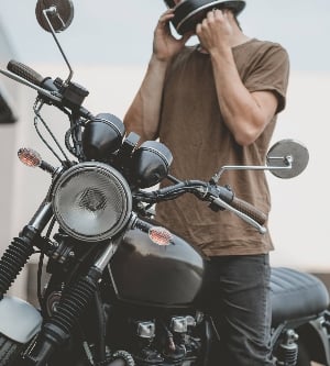 Imagen de un chico guapo jinete motorista con casco negro y sentado en una motocicleta café racer de estilo clásico. Bicicleta a medida en garaje vintage. Estilo de vida urbano brutal y divertido. Retrato al aire libre.