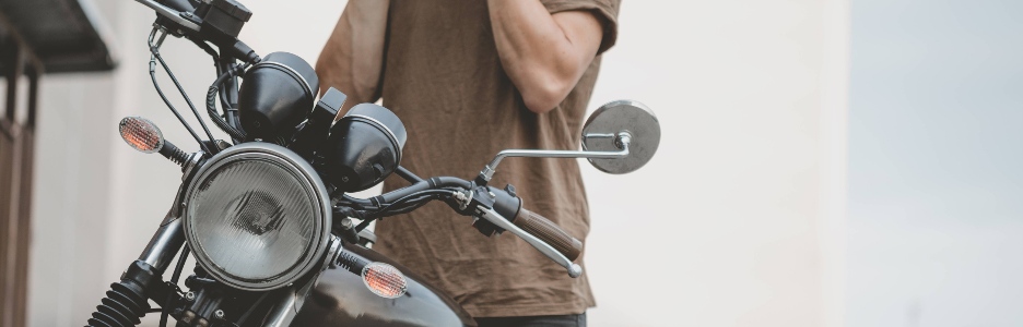 Imagen de un chico guapo jinete motorista con casco negro y sentado en una motocicleta café racer de estilo clásico. Bicicleta a medida en garaje vintage. Estilo de vida urbano brutal y divertido. Retrato al aire libre.