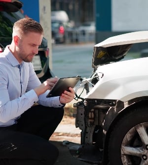 Imagen de un hombre con camisa blanca inspecciona un coche tras un accidente para reclamar el seguro.