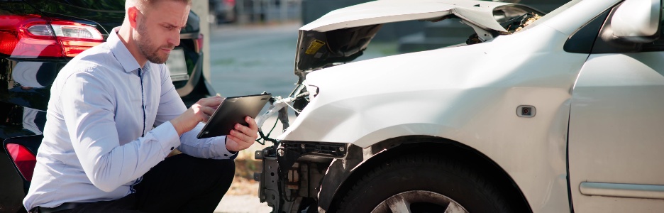 Imagen de un hombre con camisa blanca inspecciona un coche tras un accidente para reclamar el seguro.