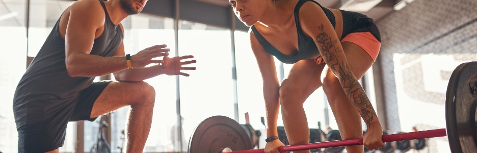 Imagen de parte inferior del entrenador diciéndole a la chica haciendo peso muerto
