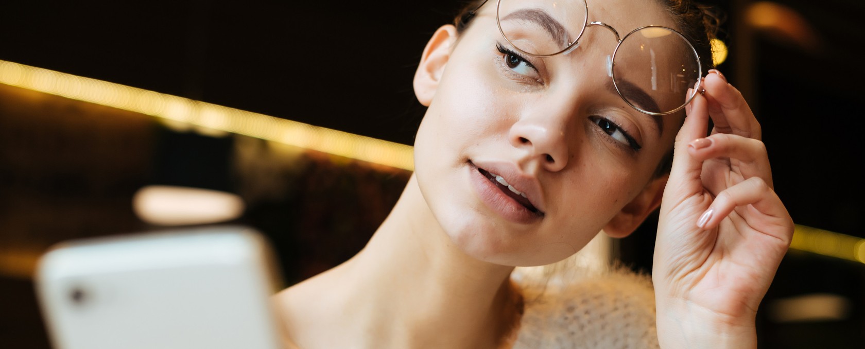 Imagen de linda joven estudiante con anteojos se sienta en un café después de un uchpeba y mantiene el teléfono inteligente