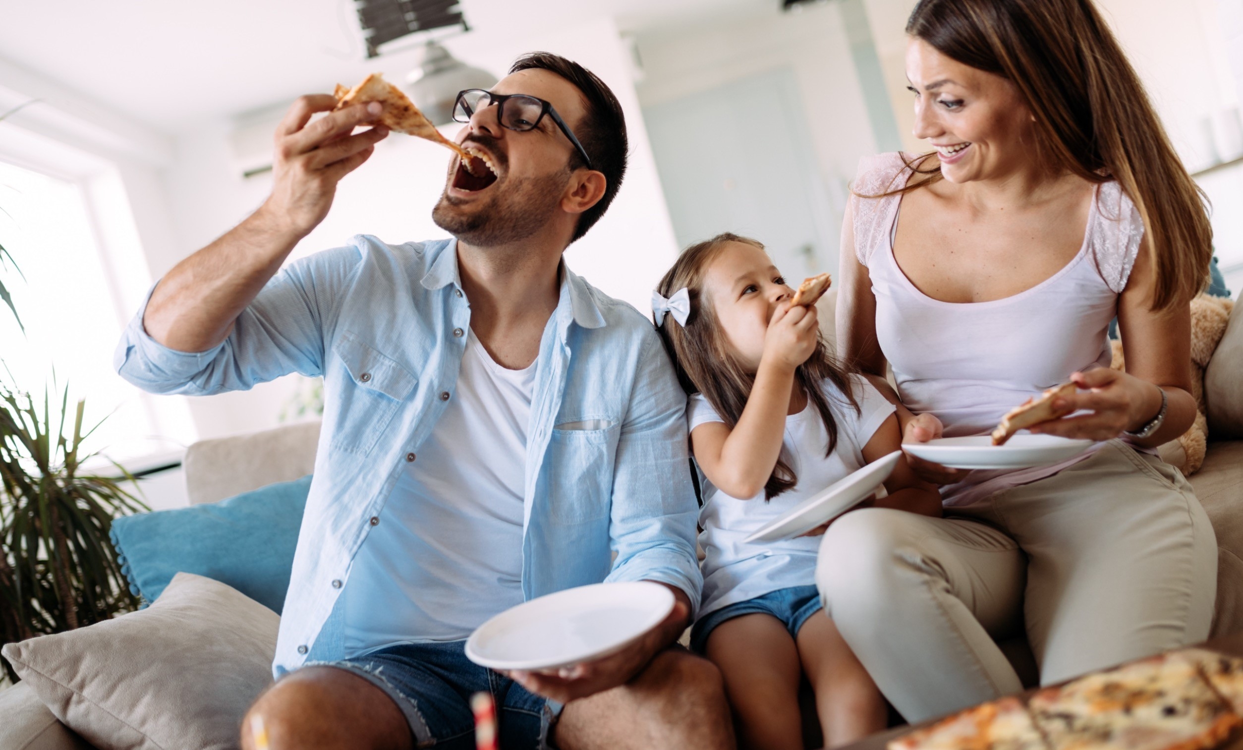 Imagen de una familia comiendo una pizza en el sofá juntos