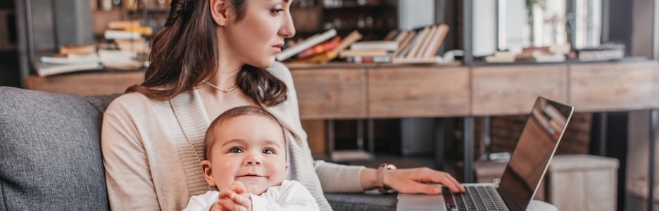 Imagen de madre sentada en el sofá con su hijo y usando la computadora portátil en casa