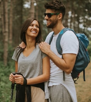 Imagen de pareja joven sonriente caminando con mochilas en el bosque en un día de verano